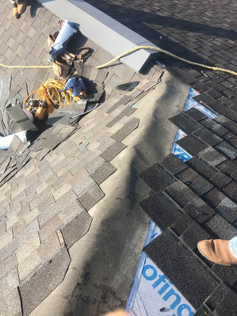 Roofer replacing shingles damaged by another trade near a roof vent at Creekside Elementary School in Franklin, Tennessee
