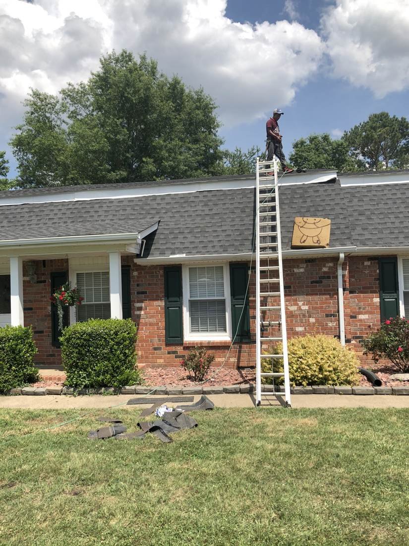 Roofer working on a hip roof during a tear-off and reroof on a home in Middle Tennessee, with a ladder and removed shingle debris on the lawn