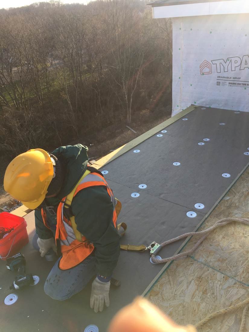 Roofer fastening insulation board with plates on a flat roof apartment building in Knoxville, Tennessee