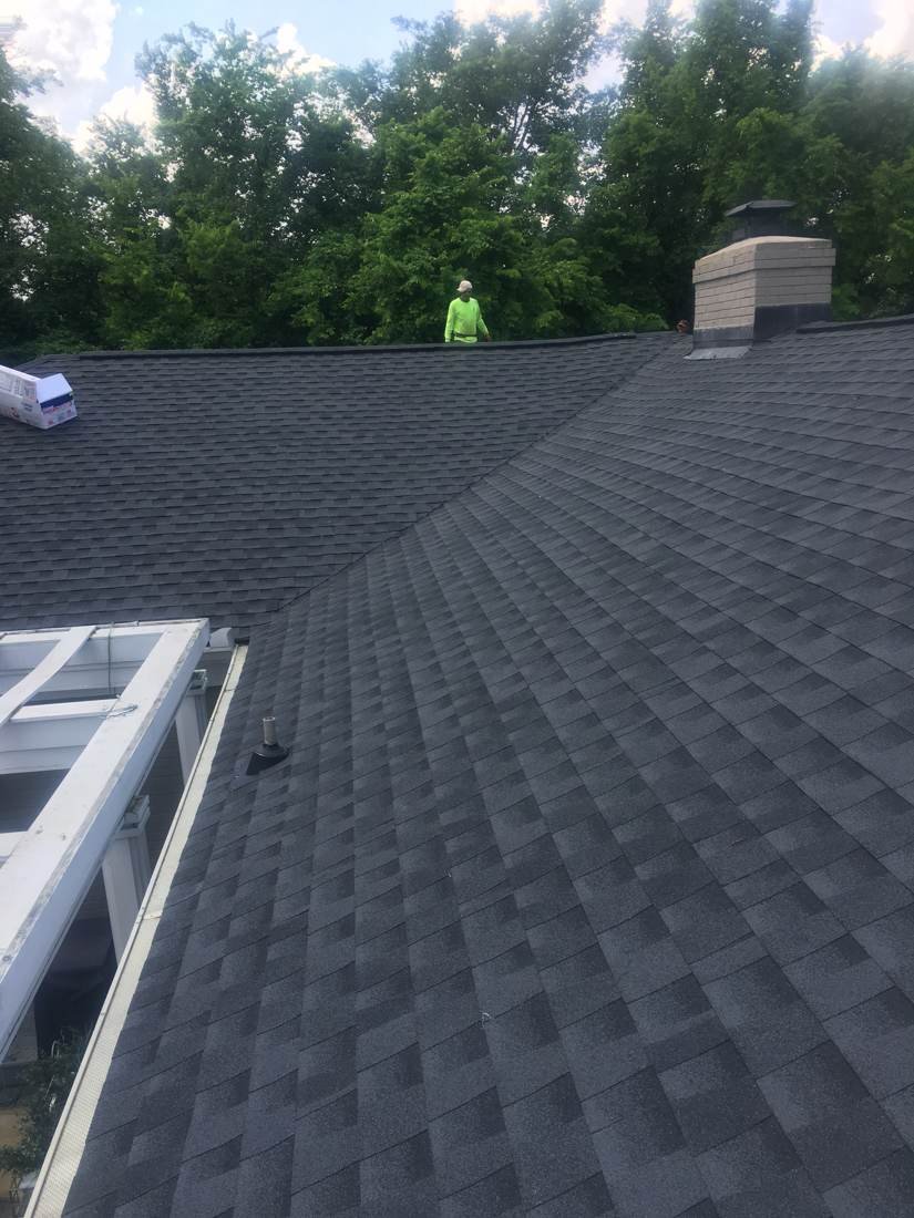 Crew member finishing shingle installation near a roof vent