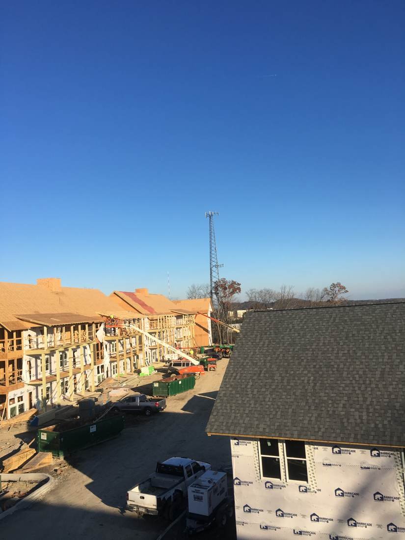 Wide view of roof framing and decking work on new-construction apartment buildings near downtown Nashville, Tennessee, with a boom lift on site