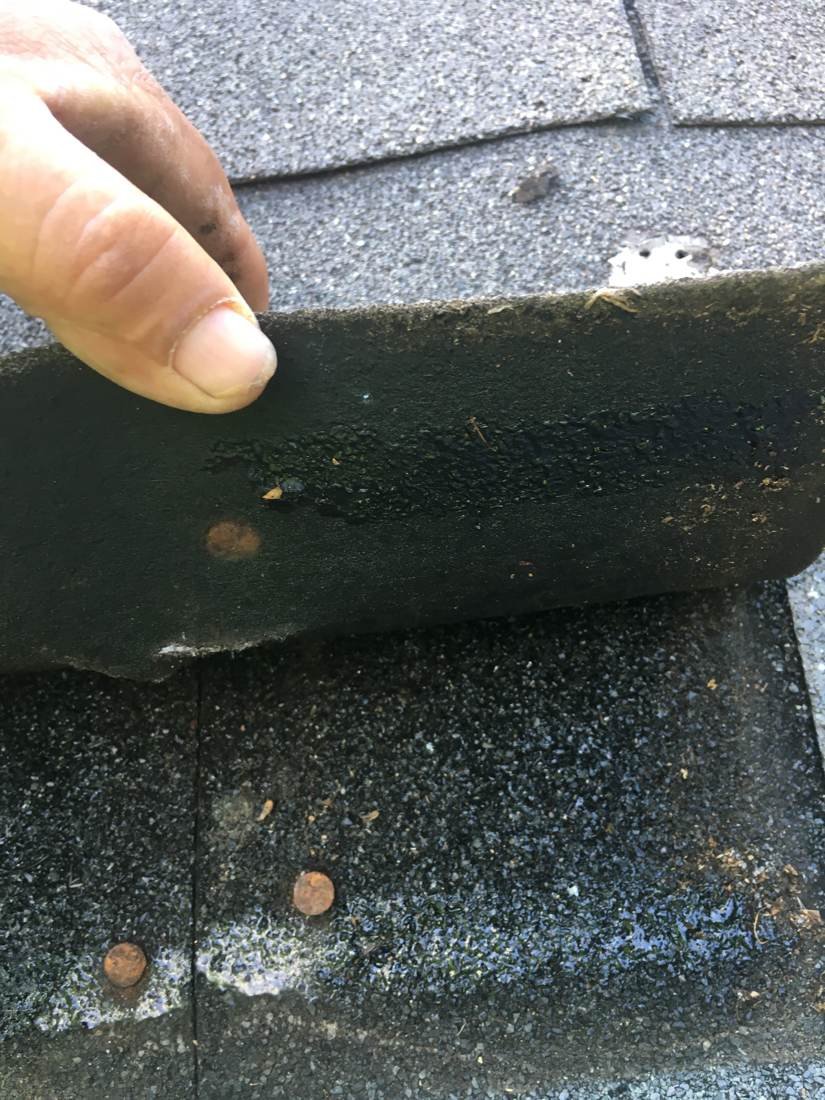 Exposed, unsealed nail heads found under a lifted shingle during a roof inspection