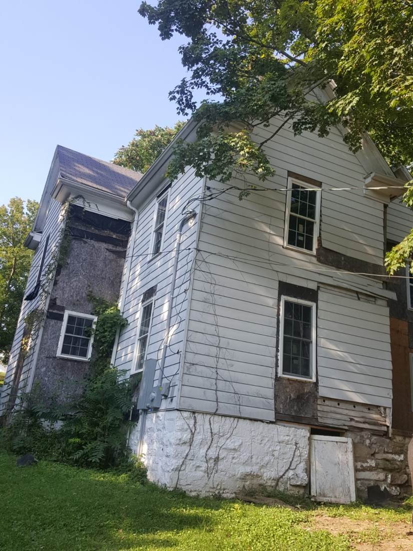 Siding removed from farmhouse exterior revealing exposed sheathing and water-damaged trim underneath